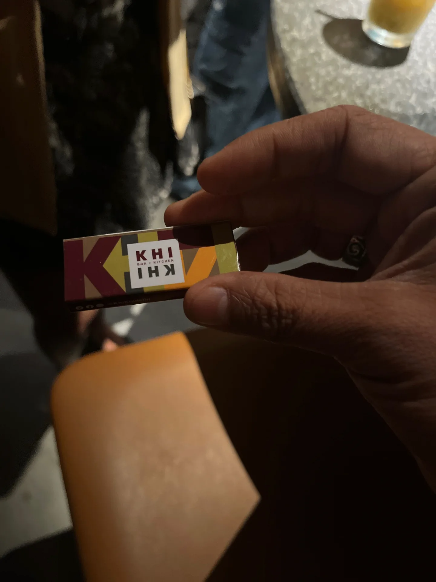KHI KHI business card being held, featuring colorful geometric pattern and logo design