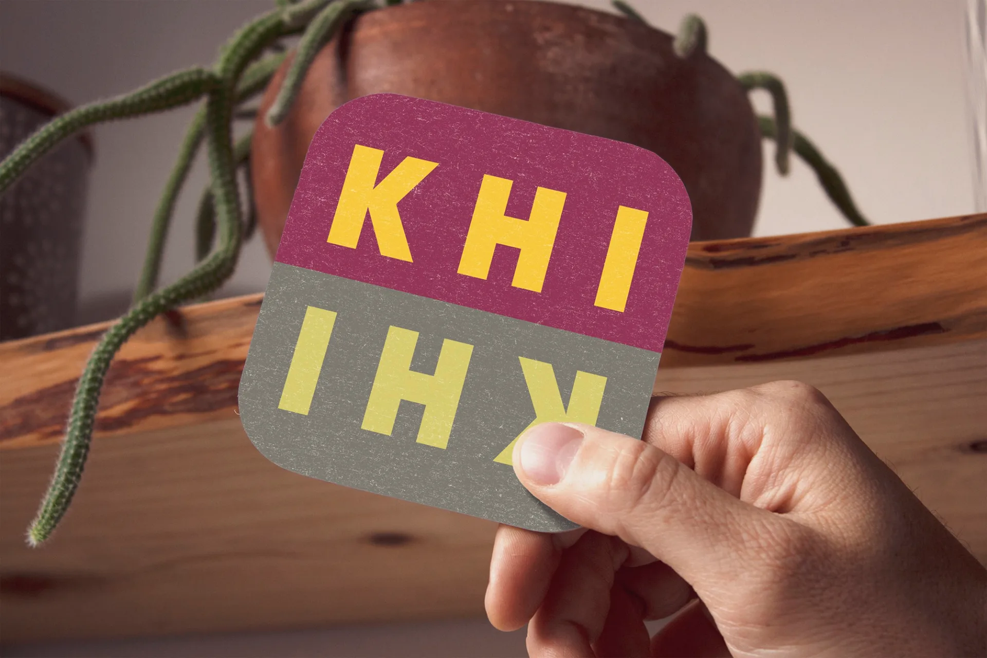 KHI KHI branded coaster with burgundy and olive green logo held in hand, showcasing restaurant table accessories