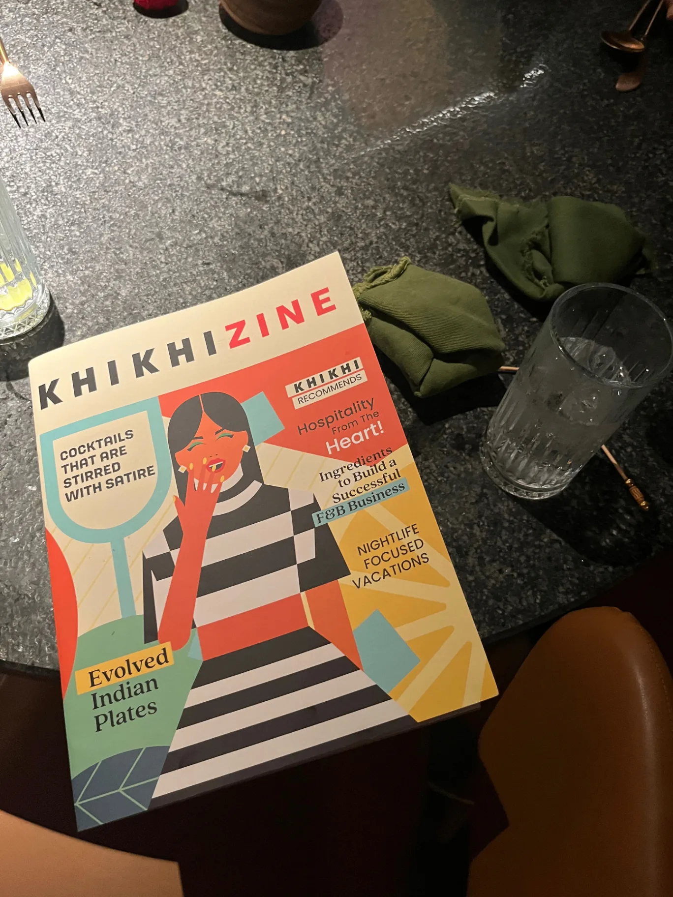 KHIKHIZINE magazine on restaurant table featuring illustrated cover with colorful brand identity and cocktail theme