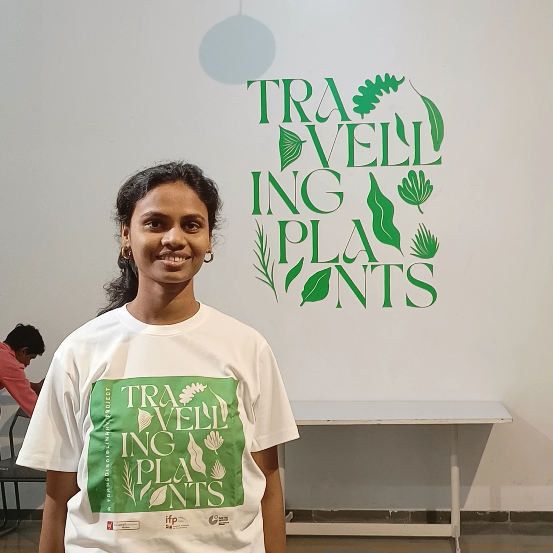 Exhibition visitor wearing Travelling Plants branded t-shirt in front of green botanical wall typography display